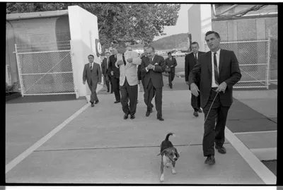 Secret Service agent Lem Johns, with a beagle dog on a leash, leads President Lyndon B. Johnson and party to the USS Sequoia for a dinner cruise with foreign ambassadors. Cruise on the Sequoia, 12 August 1965.